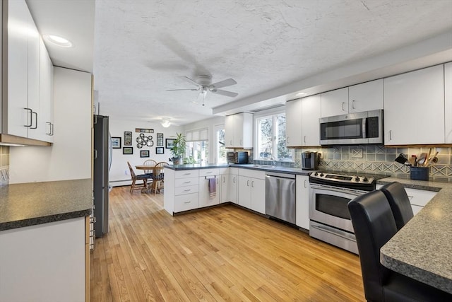 kitchen with light wood-type flooring, a ceiling fan, appliances with stainless steel finishes, a peninsula, and white cabinets