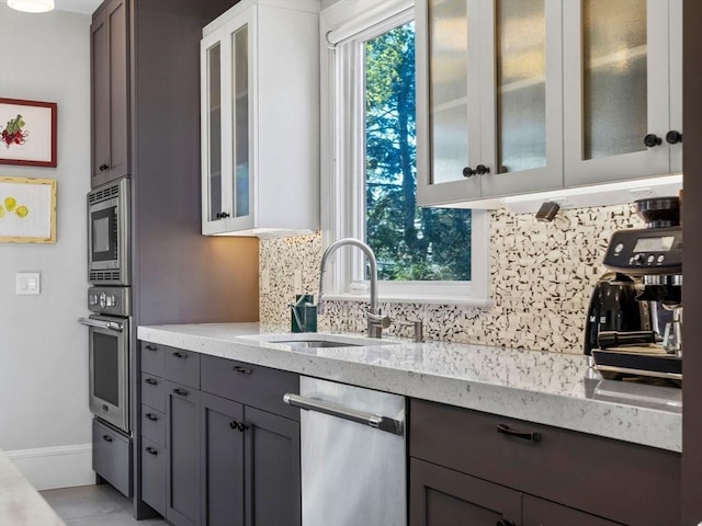 kitchen featuring light stone countertops, appliances with stainless steel finishes, a sink, gray cabinets, and tasteful backsplash