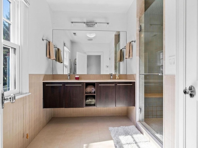 full bathroom with a sink, double vanity, tile patterned floors, a wainscoted wall, and a stall shower
