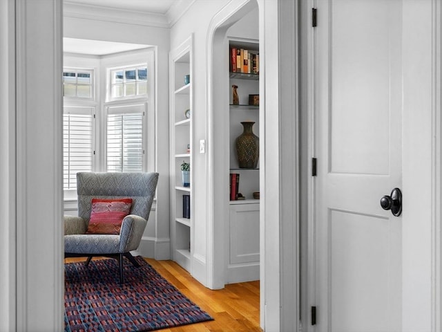 living area featuring built in shelves, ornamental molding, and light wood-style flooring