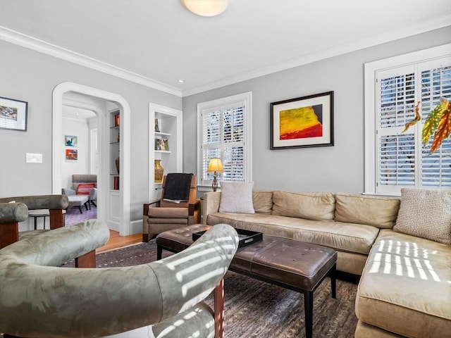 living area featuring arched walkways, built in features, ornamental molding, and wood finished floors