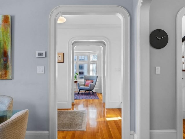 corridor with arched walkways, baseboards, and wood finished floors
