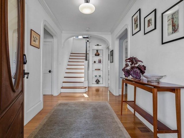 foyer with stairway, arched walkways, ornamental molding, and wood finished floors