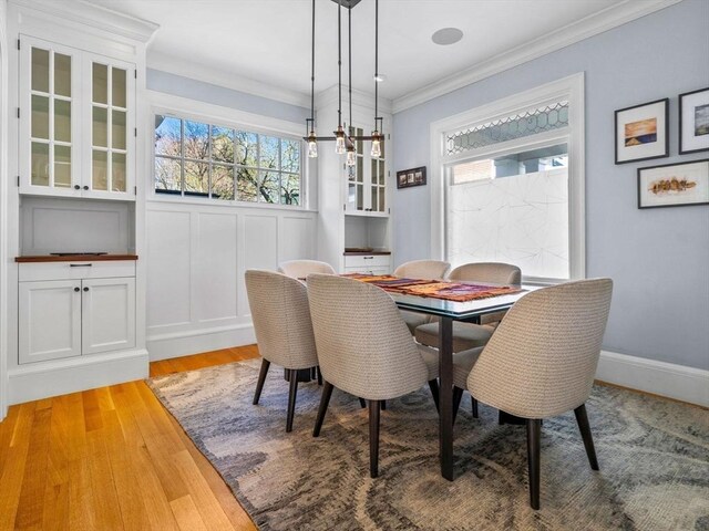 dining space featuring light wood-style floors, ornamental molding, a decorative wall, and a wealth of natural light