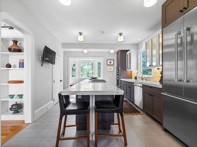 kitchen featuring a kitchen island, light tile patterned floors, appliances with stainless steel finishes, and a sink
