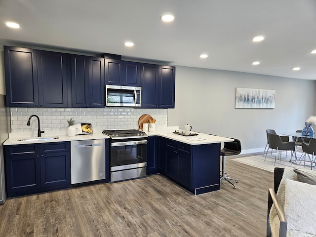 kitchen with stainless steel appliances, hardwood / wood-style flooring, sink, kitchen peninsula, and a breakfast bar area