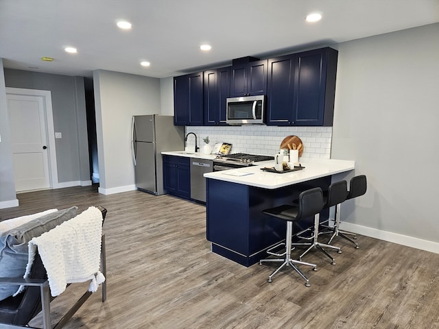 kitchen with light wood-type flooring, appliances with stainless steel finishes, sink, a kitchen breakfast bar, and kitchen peninsula