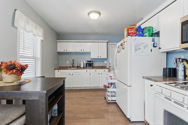 kitchen with dark countertops, white range with gas stovetop, white cabinets, a sink, and light wood finished floors