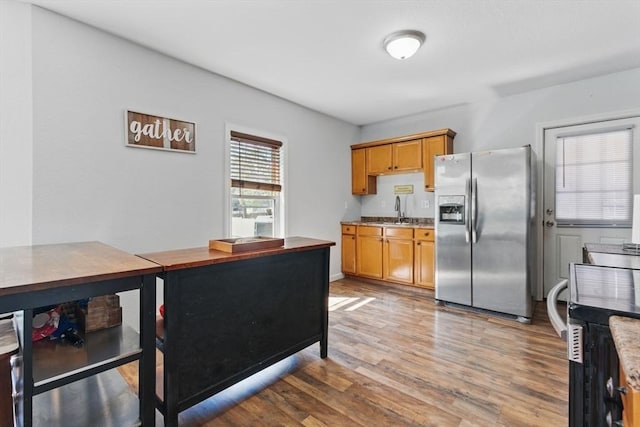 kitchen featuring stainless steel refrigerator with ice dispenser, brown cabinets, light wood-type flooring, a sink, and light countertops
