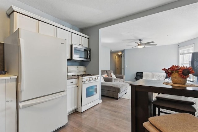 kitchen with white appliances, open floor plan, ceiling fan, white cabinets, and light wood-style flooring