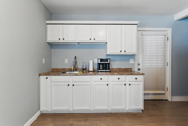 kitchen featuring baseboards, a sink, white cabinetry, and dark countertops