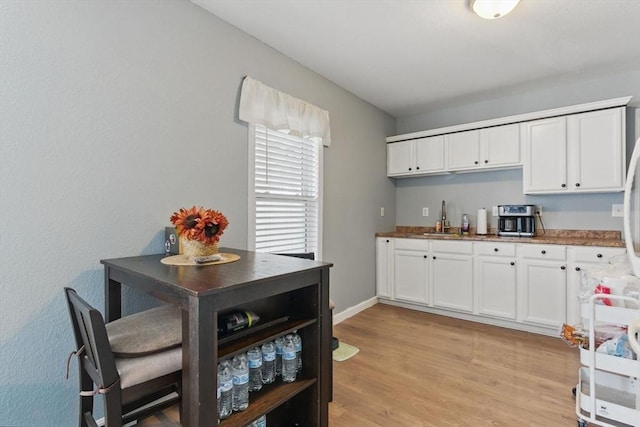 kitchen featuring white cabinetry, baseboards, a sink, and light wood finished floors