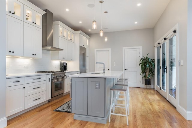 kitchen featuring pendant lighting, wall chimney range hood, a kitchen island with sink, high quality appliances, and white cabinets