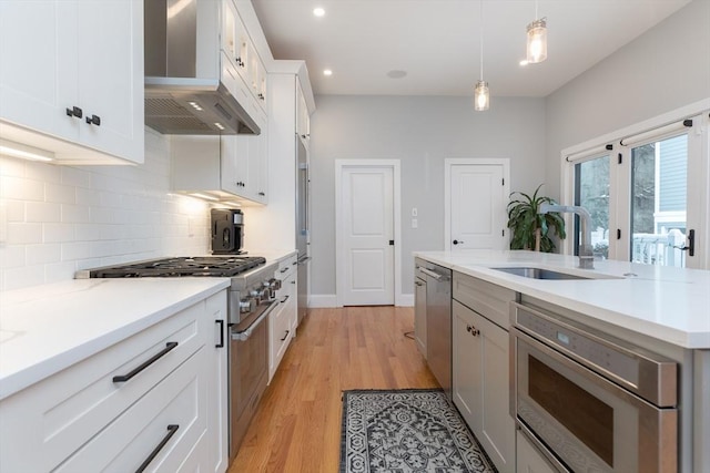 kitchen featuring extractor fan, high quality appliances, white cabinetry, sink, and hanging light fixtures