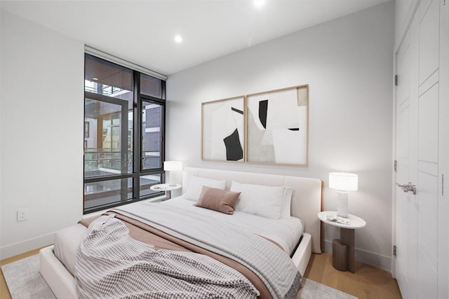 bedroom with baseboards, wood finished floors, access to outside, expansive windows, and recessed lighting