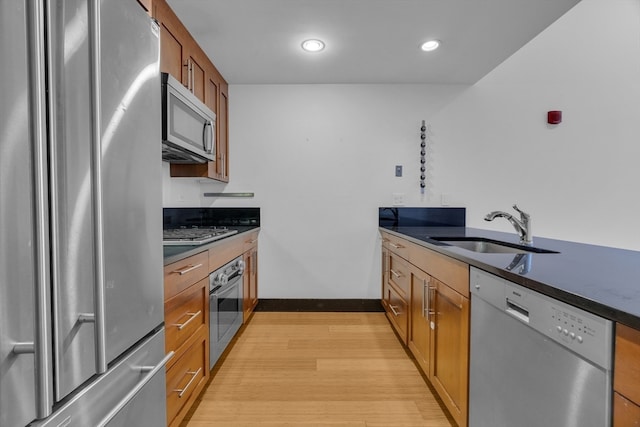 kitchen featuring light wood-type flooring, dark stone countertops, stainless steel appliances, and sink