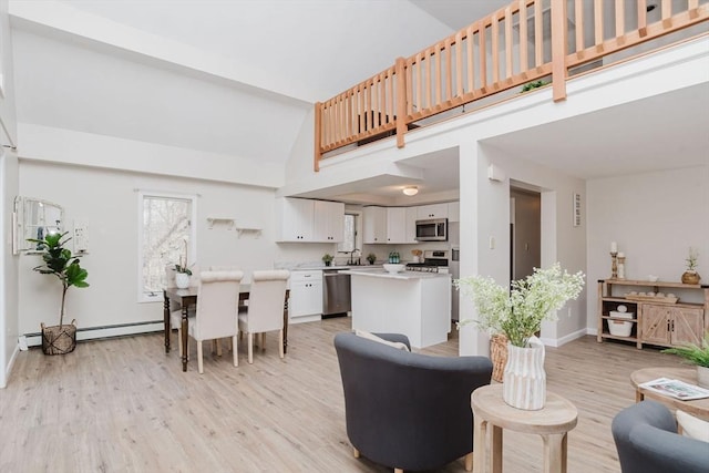 living area with a baseboard heating unit, high vaulted ceiling, light wood-style flooring, and baseboards