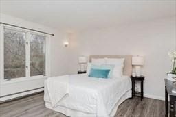 bedroom featuring a baseboard heating unit, wood finished floors, and baseboards