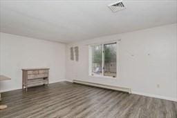 empty room with a baseboard heating unit, visible vents, and wood finished floors