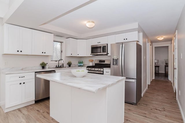 kitchen featuring light wood-style flooring, stainless steel appliances, a sink, white cabinets, and a center island