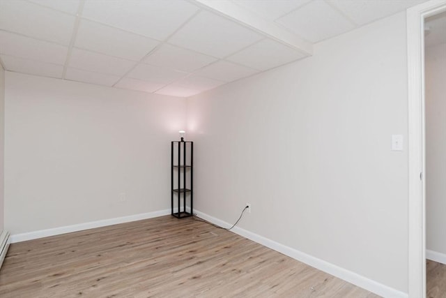 spare room featuring a baseboard radiator, light wood-type flooring, a paneled ceiling, and baseboards