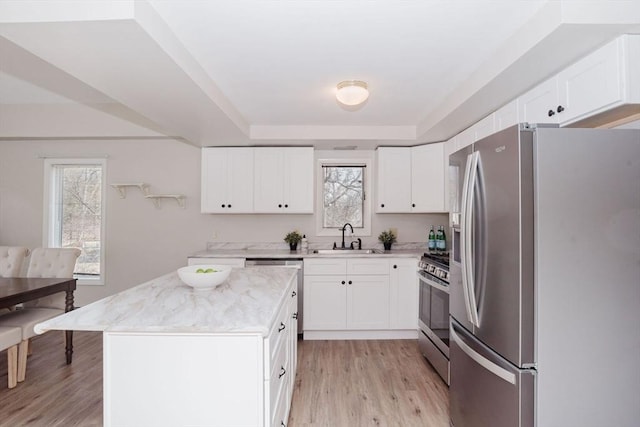 kitchen with appliances with stainless steel finishes, a healthy amount of sunlight, a sink, and light wood finished floors