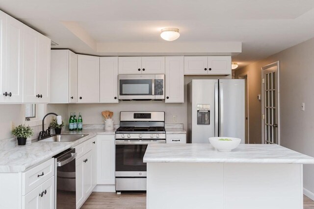 kitchen with a kitchen island, appliances with stainless steel finishes, light wood-type flooring, white cabinetry, and a sink