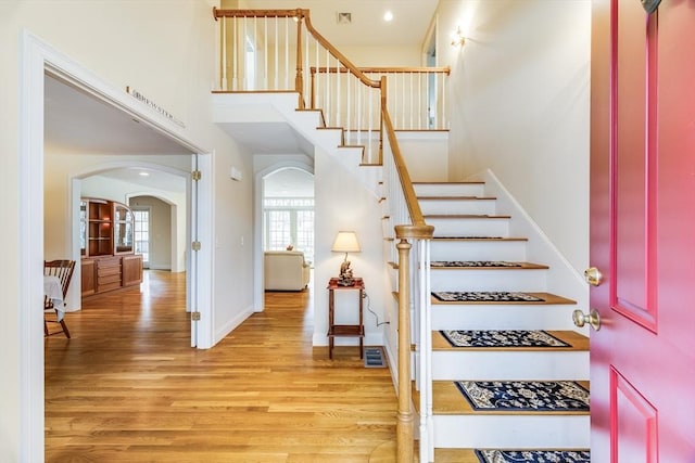 staircase with baseboards, visible vents, arched walkways, a towering ceiling, and wood finished floors