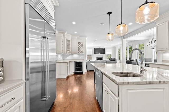 kitchen with a sink, stainless steel appliances, beverage cooler, and white cabinetry