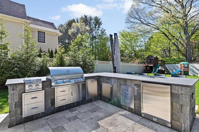 view of patio featuring a playground, fence, an outdoor kitchen, and a grill