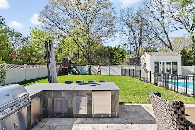 view of patio / terrace with grilling area, a fenced backyard, a playground, exterior kitchen, and an outbuilding