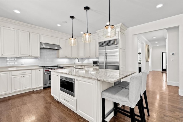 kitchen featuring wall chimney range hood, premium appliances, a sink, and dark wood-type flooring
