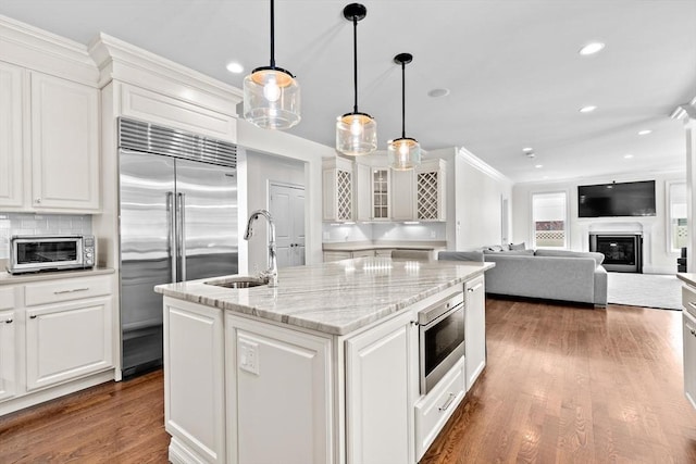 kitchen featuring white cabinets, a sink, built in appliances, a toaster, and a center island with sink