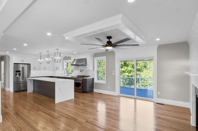 kitchen with white cabinetry, a center island, appliances with stainless steel finishes, decorative backsplash, and wall chimney range hood