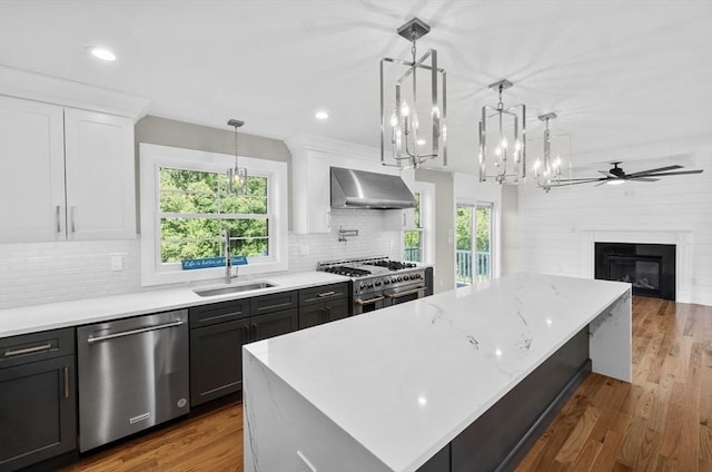 kitchen with stainless steel appliances, sink, hanging light fixtures, and wall chimney range hood