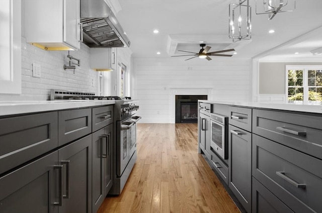 kitchen with decorative light fixtures, tasteful backsplash, exhaust hood, high end stainless steel range, and light wood-type flooring