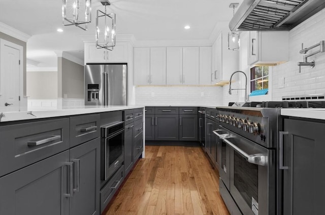 kitchen with white cabinetry, crown molding, high end appliances, hanging light fixtures, and wall chimney range hood