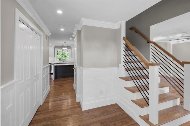 stairway with wood-type flooring, ornamental molding, and an inviting chandelier