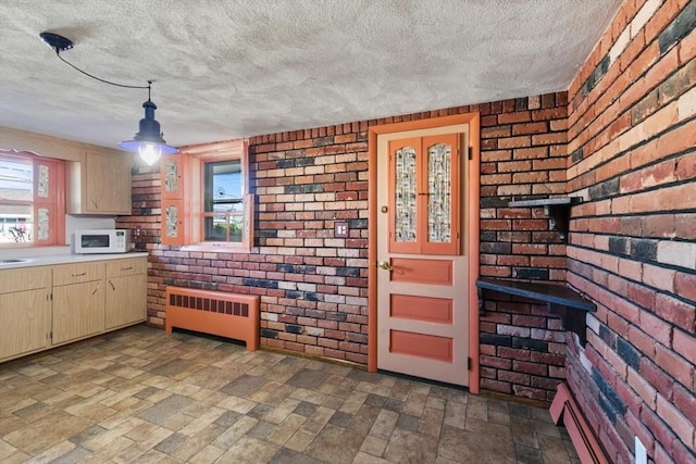 kitchen with decorative light fixtures, radiator, plenty of natural light, and brick wall