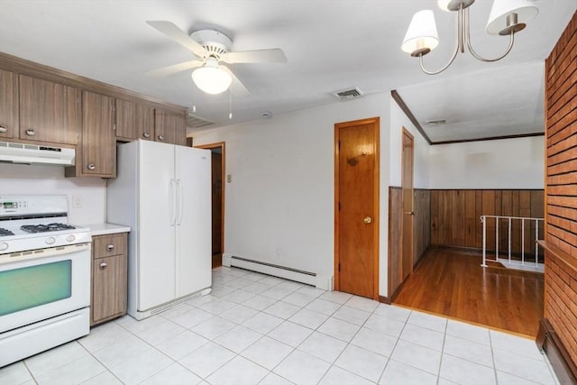 kitchen with wooden walls, a baseboard heating unit, white appliances, light tile patterned flooring, and ceiling fan with notable chandelier