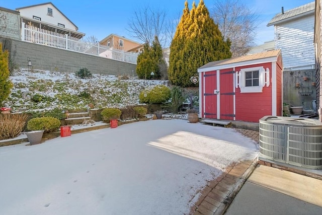 snowy yard featuring cooling unit, a storage shed, and a patio