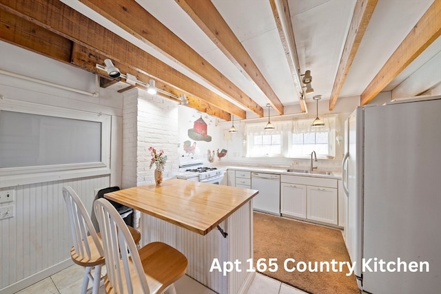 kitchen featuring white cabinetry, sink, hanging light fixtures, white appliances, and wooden walls