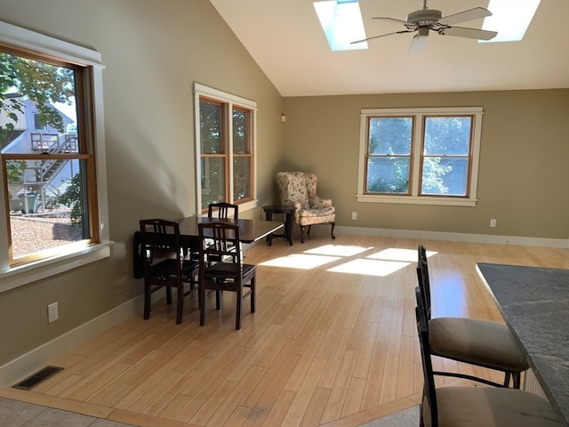 dining room with a healthy amount of sunlight, vaulted ceiling with skylight, light hardwood / wood-style floors, and ceiling fan