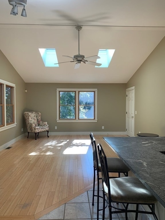 dining area featuring light hardwood / wood-style floors, lofted ceiling with skylight, and ceiling fan