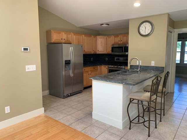 kitchen featuring a breakfast bar area, kitchen peninsula, sink, light tile patterned floors, and appliances with stainless steel finishes