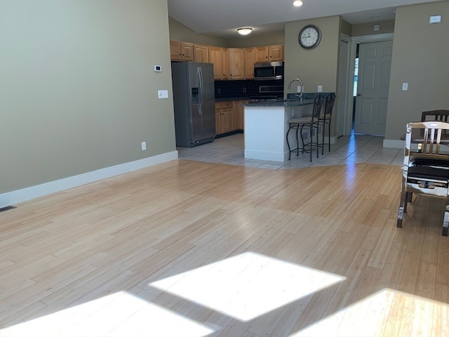 kitchen with backsplash, appliances with stainless steel finishes, a kitchen breakfast bar, light hardwood / wood-style flooring, and sink