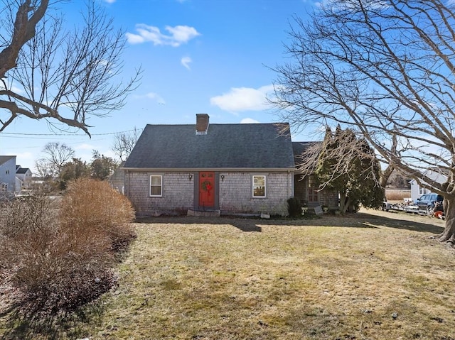 new england style home with a shingled roof, a chimney, and a front lawn