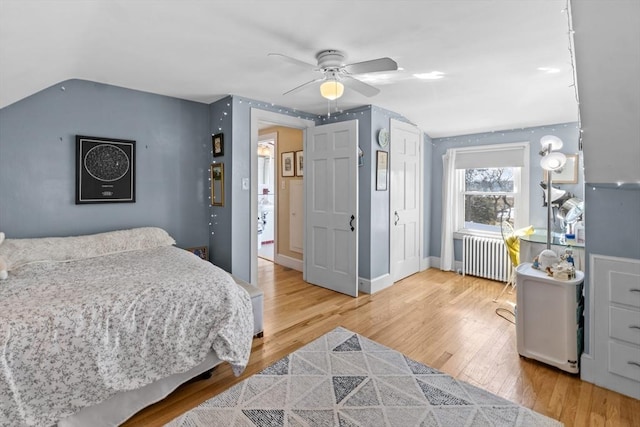 bedroom featuring lofted ceiling, radiator, light wood-style floors, ceiling fan, and baseboards