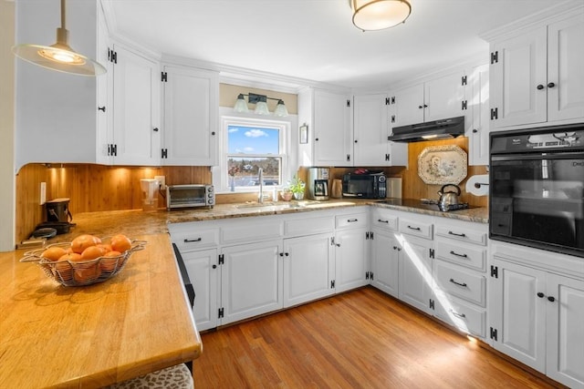 kitchen featuring decorative light fixtures, light wood-style floors, white cabinets, under cabinet range hood, and black appliances