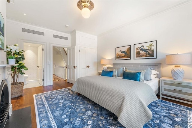 bedroom with wood finished floors, visible vents, ornamental molding, a closet, and ensuite bathroom